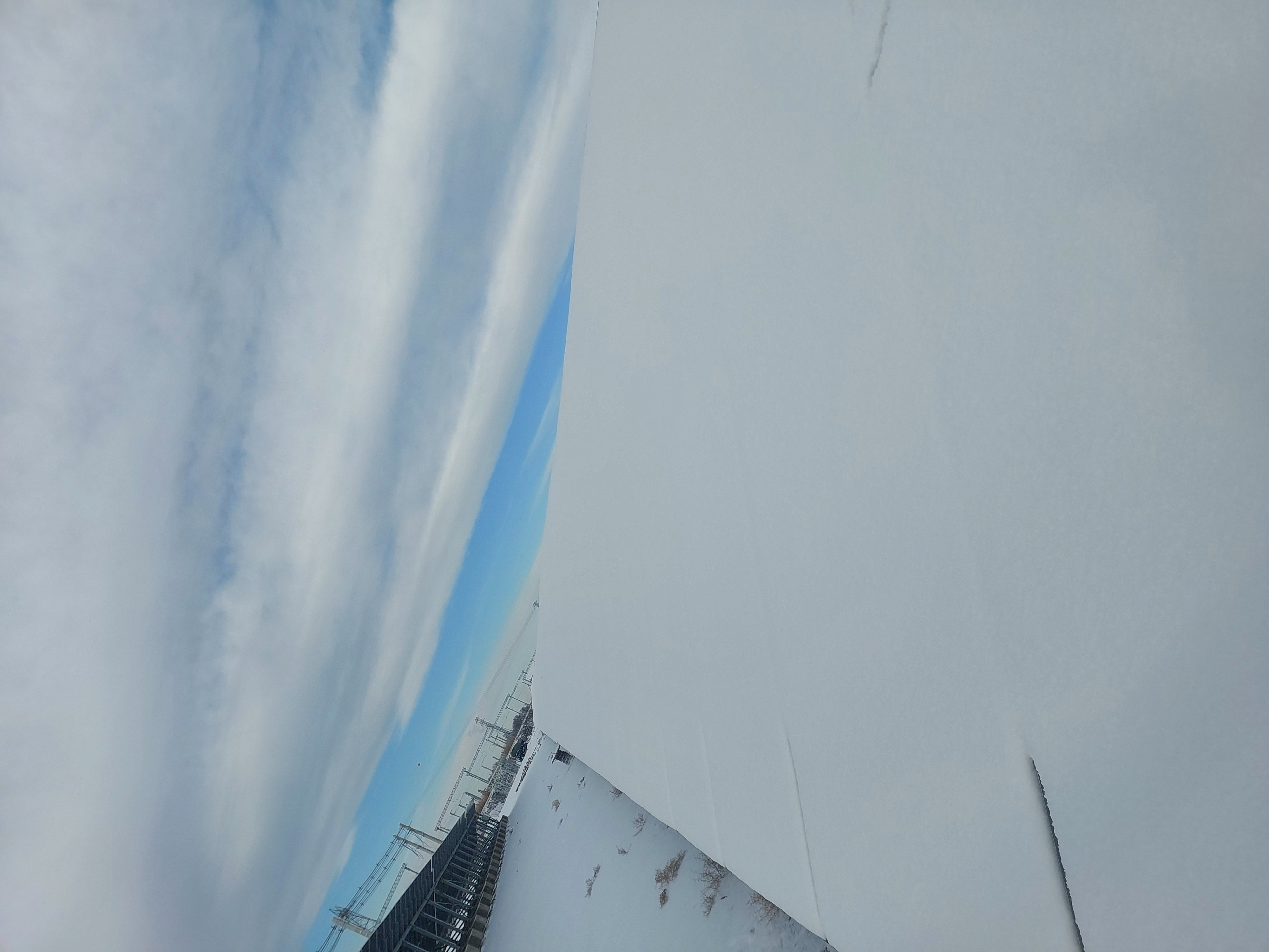 Snow-covered solar panels with a substation in the background