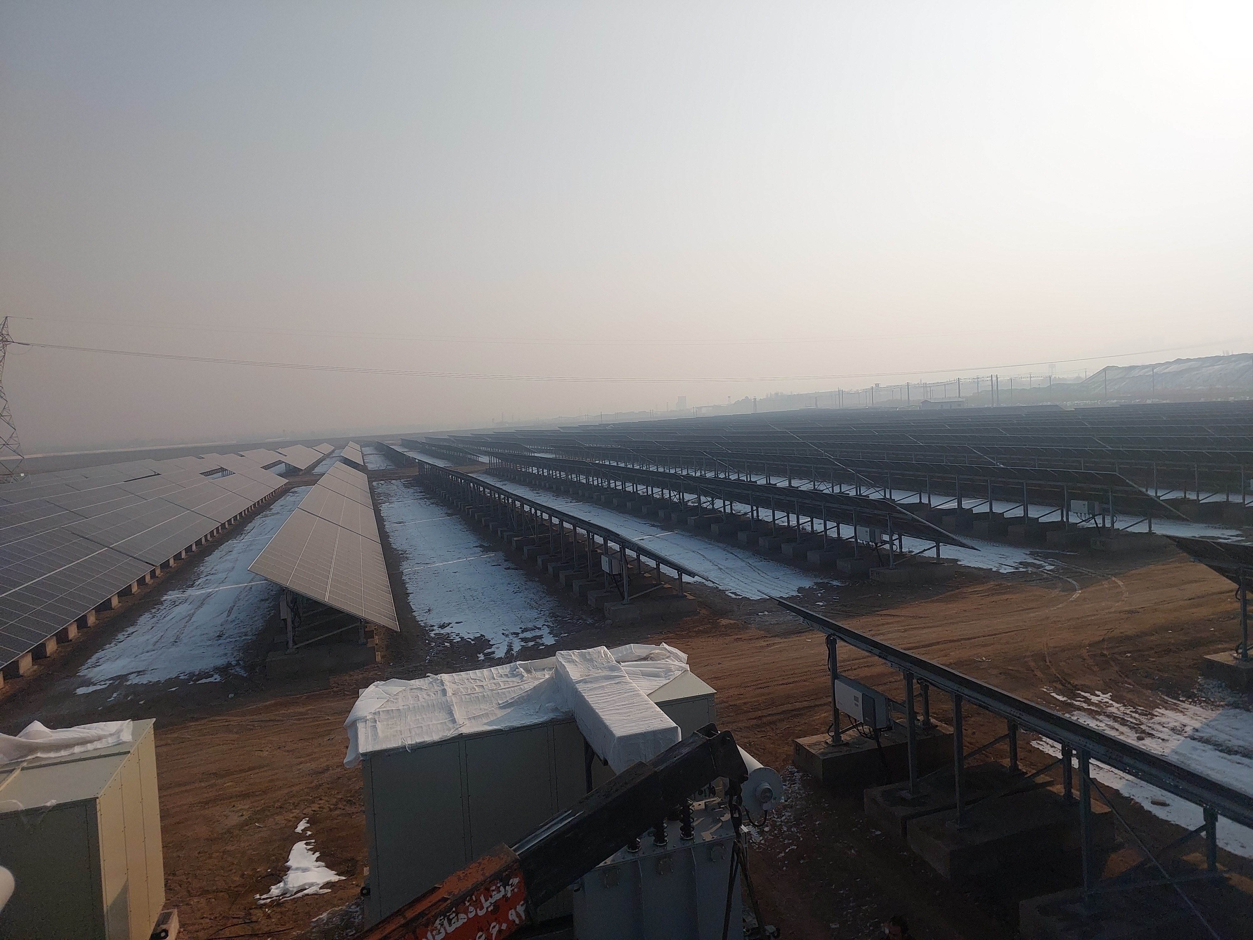 Crane installing a transformer station beside snowy solar panels